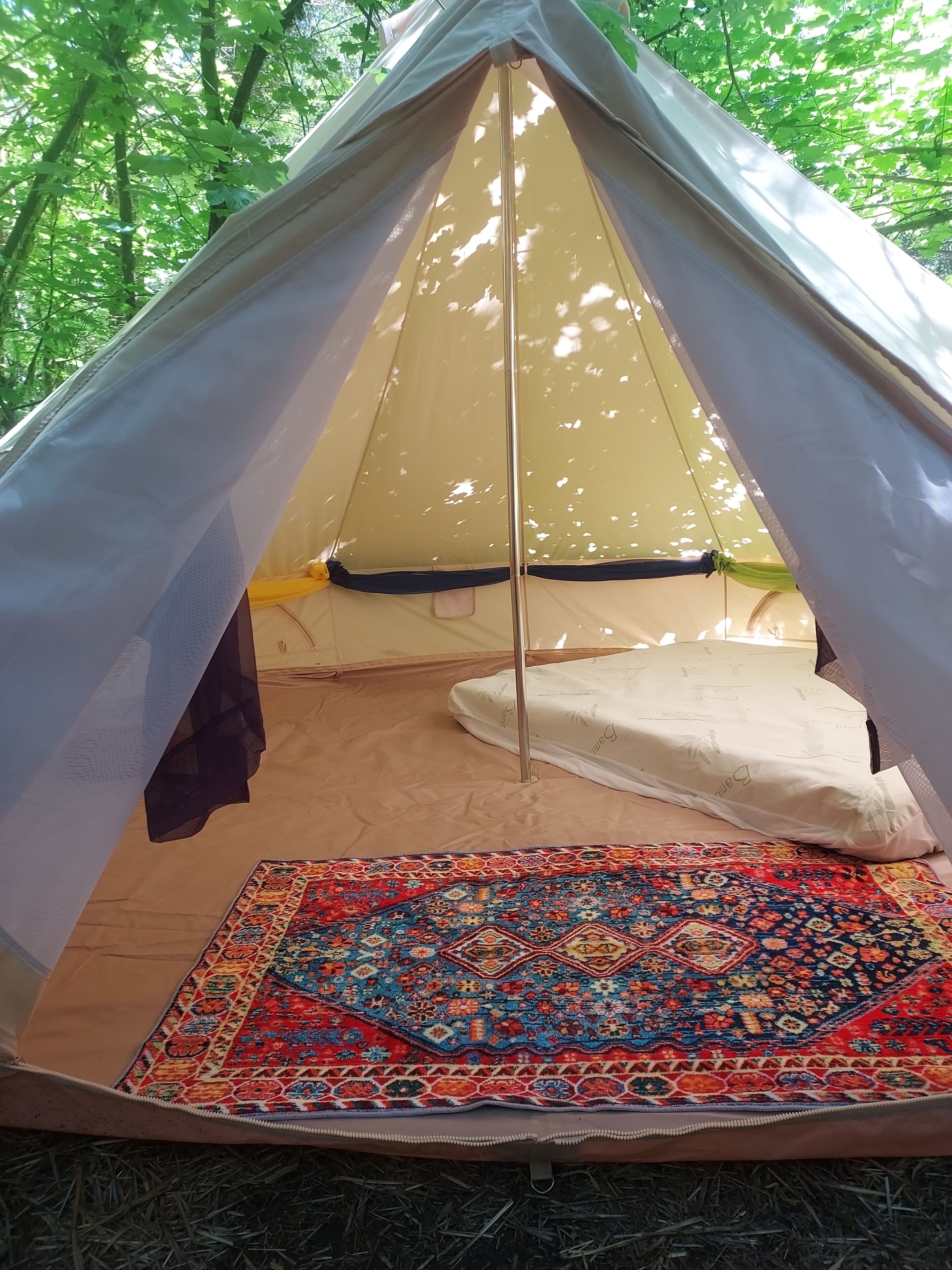 Une tente avec un tapis coloré à l’intérieur, un sac de couchage et un poteau de tente.