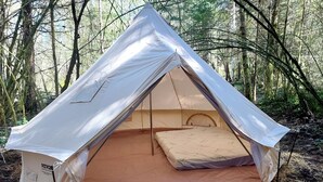 Una carpa con zona de dormir en su interior, rodeada de un bosque.
