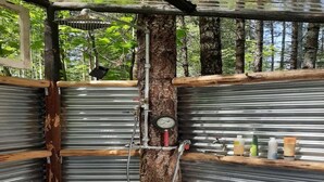 Un baño rústico con un tronco de árbol, paneles metálicos y un manómetro.