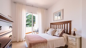 A bedroom with a bed, nightstand, dresser, and a view of the outdoors.