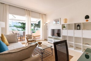 A modern living room with a sofa, armchairs, a glass coffee table, a TV, and built-in shelving.