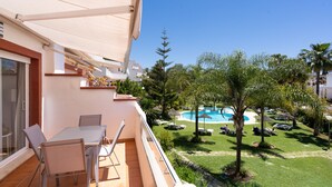 A balcony with a table and chairs, overlooking a swimming pool and lush greenery.
