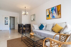 A living room with a sofa, a glass coffee table, and a dining area with chairs and a table.