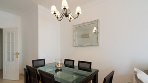 A dining area with a glass table, four chairs, a chandelier, and a mirror on the wall.
