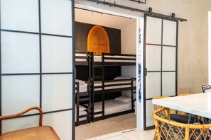 A compact room with bunk beds, a dining table, and a woven chair.