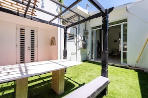 A patio with a table and bench, a white door, and a view into a room with a glass door.