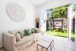 Una sala de estar moderna con un sofá color beige y un ventanal de vidrio que da a un balcón con vistas a un jardín.