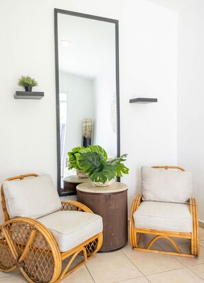 A room with two wicker chairs, a round wooden table with a plant, and a large mirror on the wall.