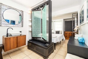 A modern bathroom with a freestanding bathtub, a wooden vanity, a large mirror, and a bed with a nightstand.