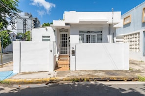 A white building with a gated entrance, a small porch, and a visible door.