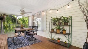 Eine überdachte Veranda mit Tisch und Stühlen, einem Deckenventilator und einem an der Wand befestigten Pflanzenregal.