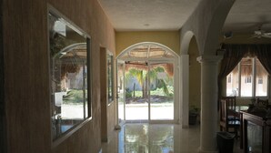 Un pasillo amplio con piso pulido que conduce a un vidrio que da a un jardín tropical.