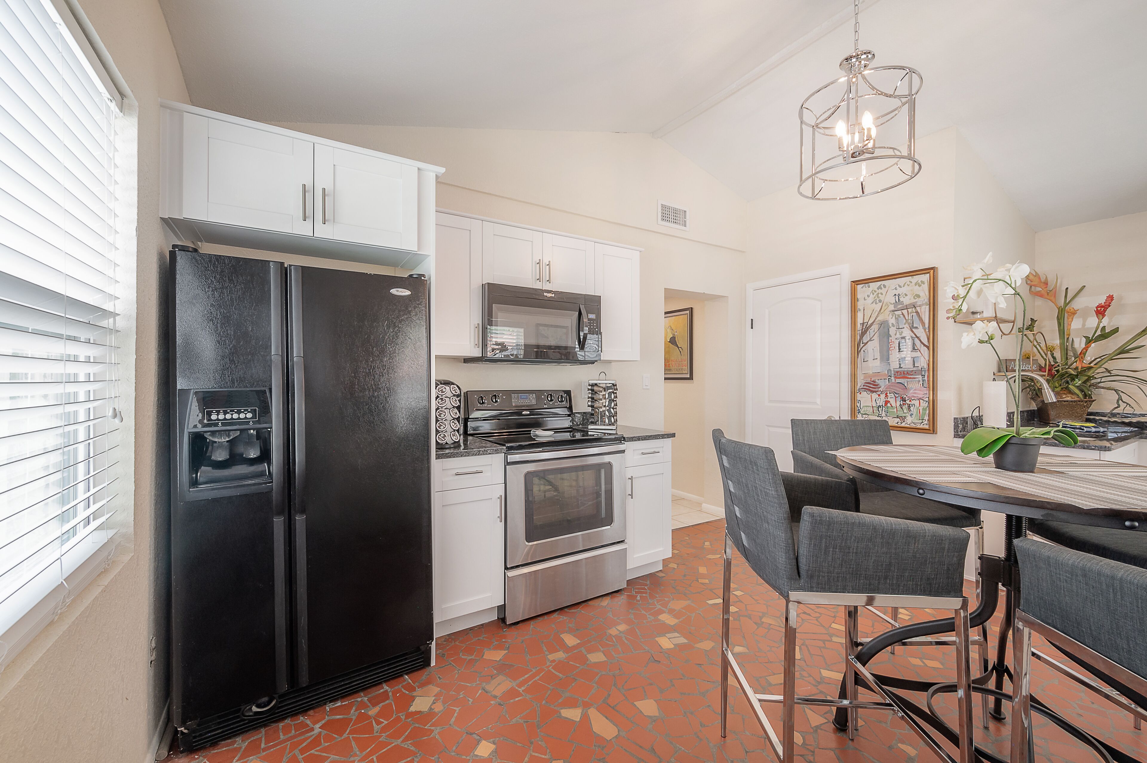 A modern kitchen with white cabinets, a black refrigerator, stainless steel appliances, and a dining area with a table and chairs.