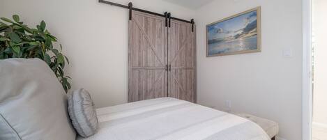 A bedroom with a bed, pillows, a plant, a painting, and a sliding door.