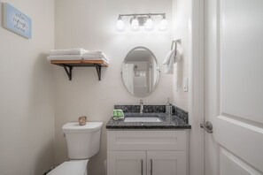 Ein Badezimmer mit Toilette, Waschbecken und Spiegel. Ein Handtuchhalter mit Handtüchern, ein Regal mit gefalteten Handtüchern und ein Schild mit der Aufschrift 'relax, refresh, renew'.