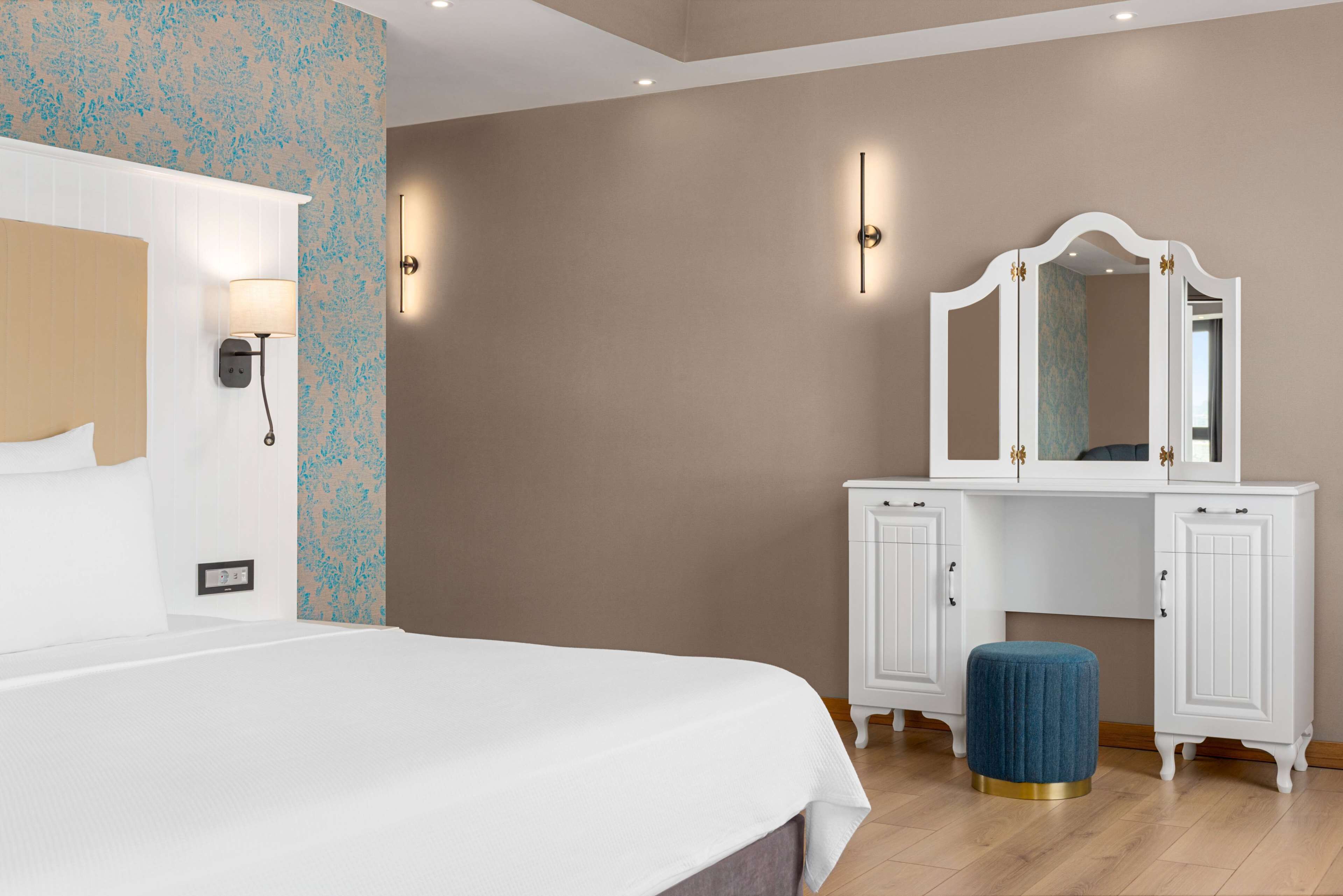 Un dormitorio con cama, cómoda, espejo y apliques de pared.