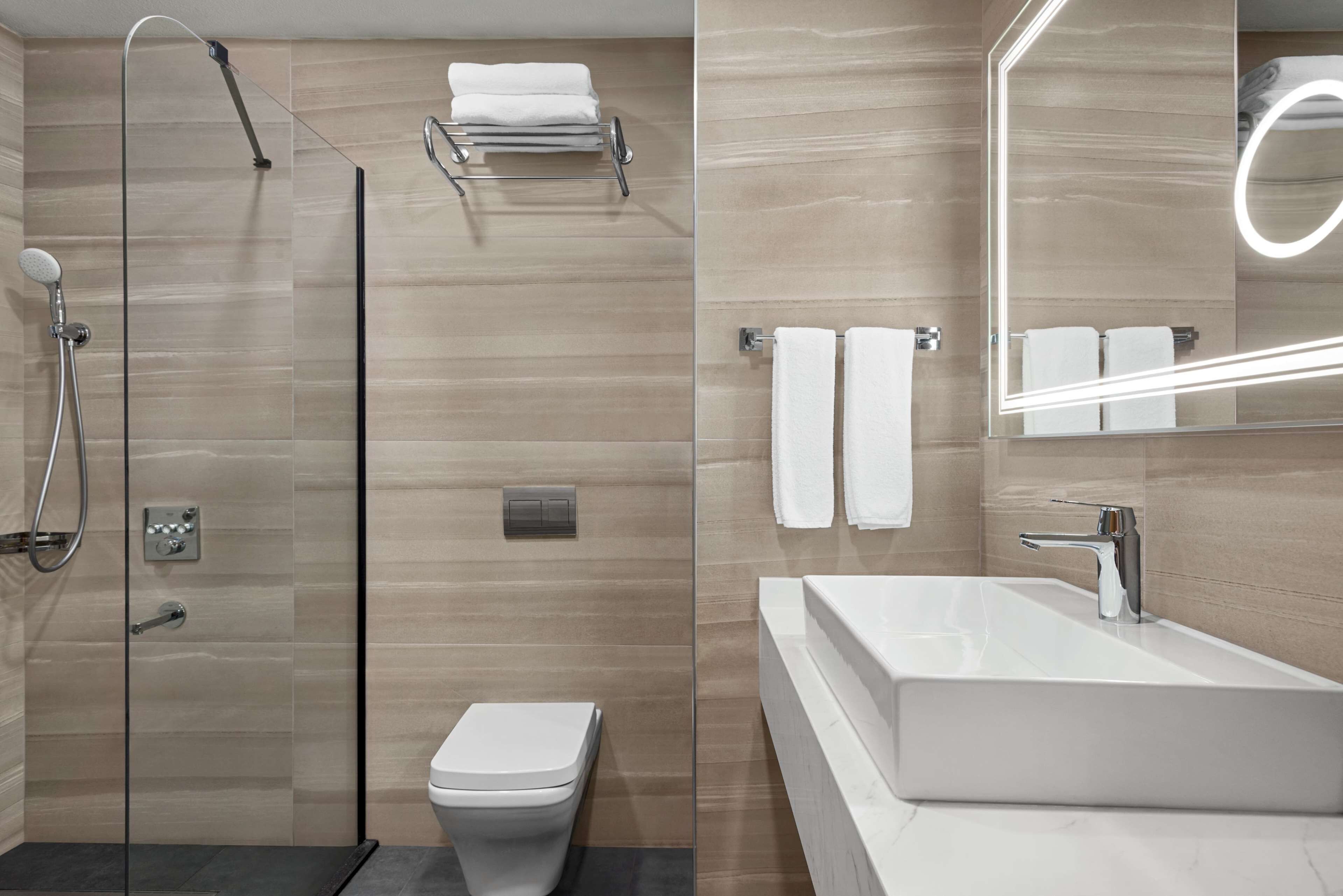 A modern bathroom with a glass-enclosed shower, a white toilet, a vanity with a large mirror, and a built-in bathtub.
