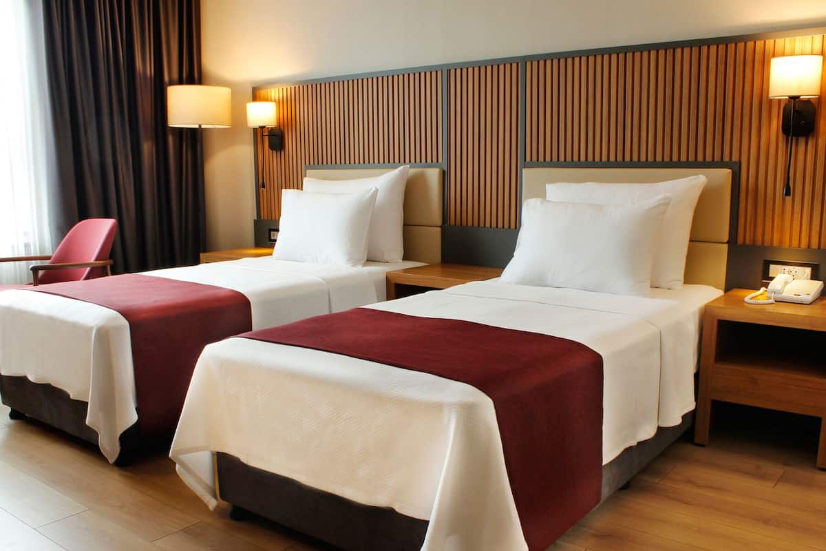Ein Hotelzimmer mit zwei Betten, jeweils mit einer roten und weißen Tagesdecke, Holzkopfteilen und Nachttischlampen.