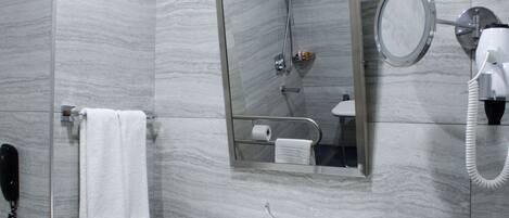 A bathroom with a marble wall, a sink, a mirror, a handheld showerhead, a towel, and a telephone.