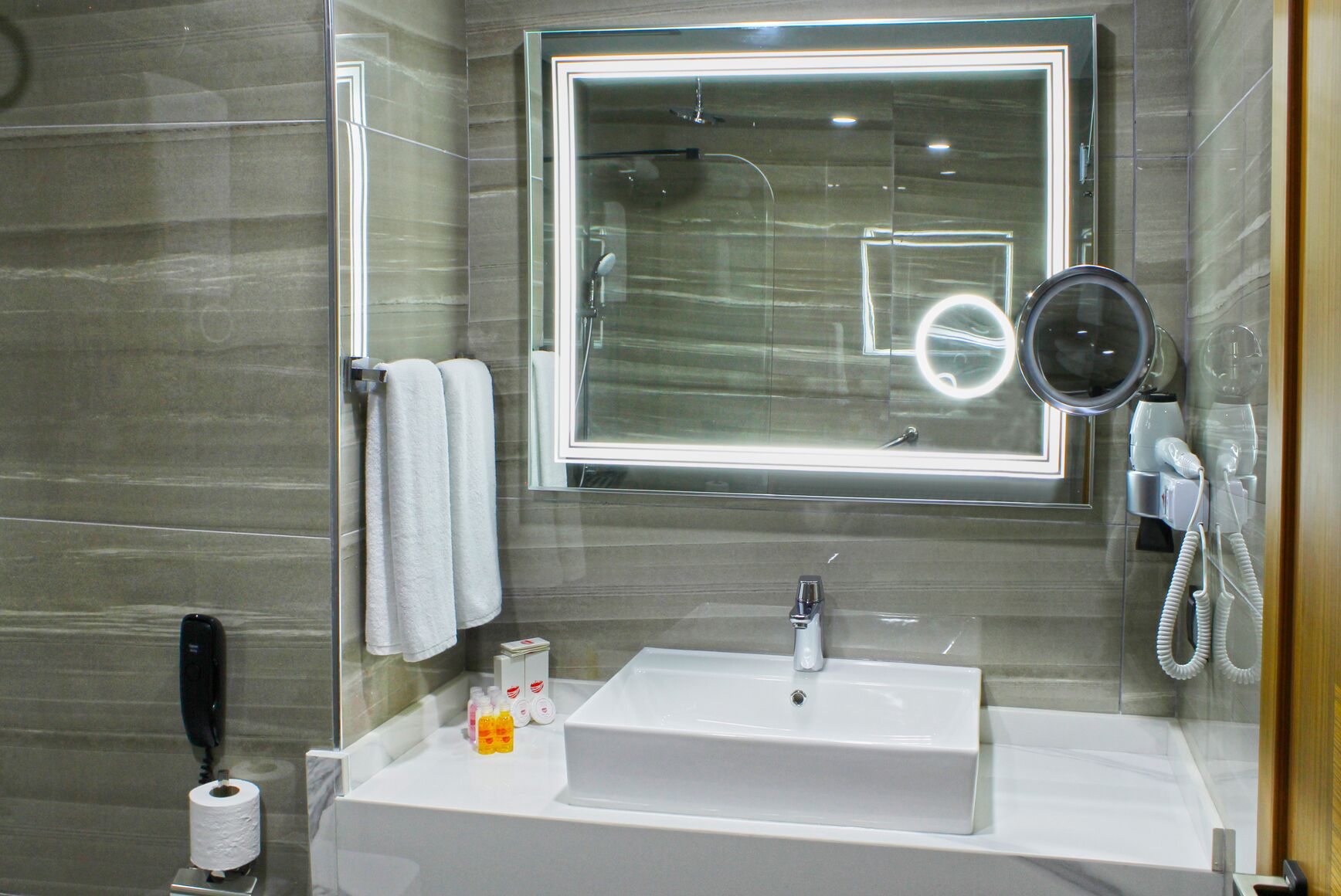 Un baño moderno con un espejo rectangular, un lavabo blanco y un cabezal de ducha de mano.