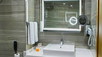 Un baño moderno con un espejo rectangular, un lavabo blanco y un cabezal de ducha de mano.