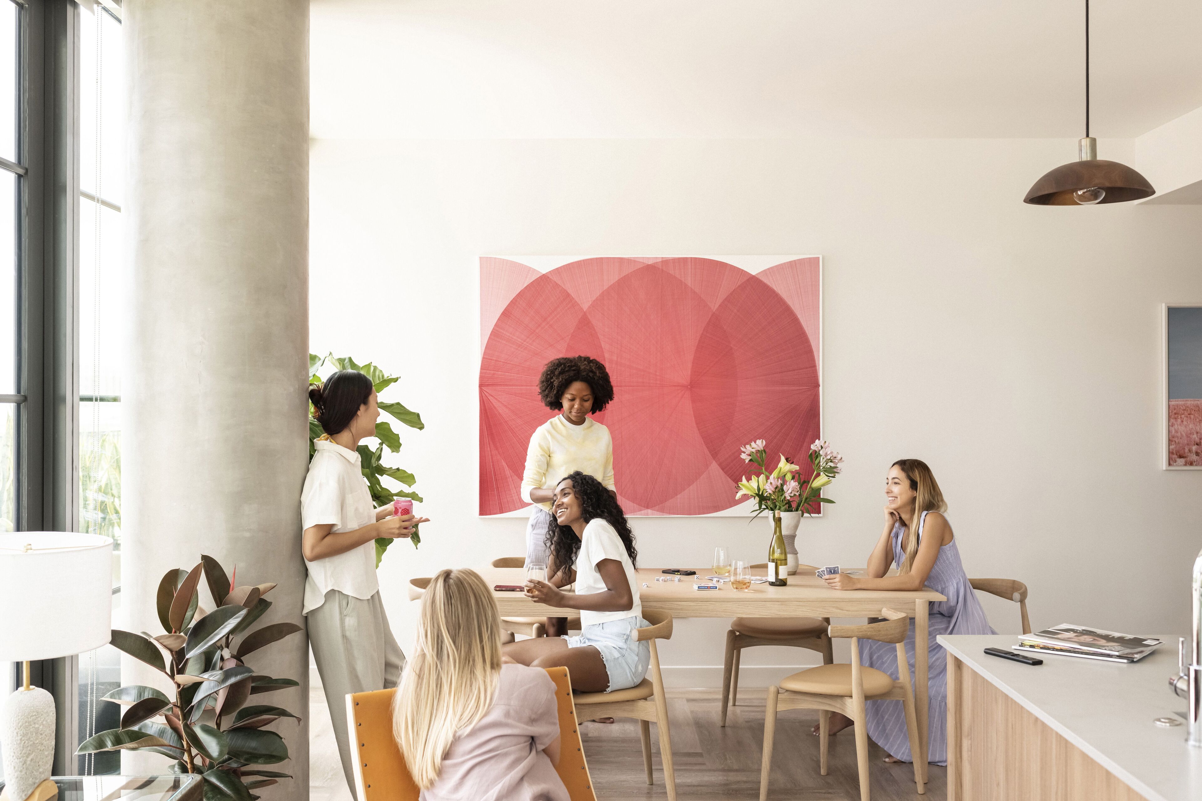 A modern meeting room with a large abstract painting, a wooden table, and a few seated individuals.