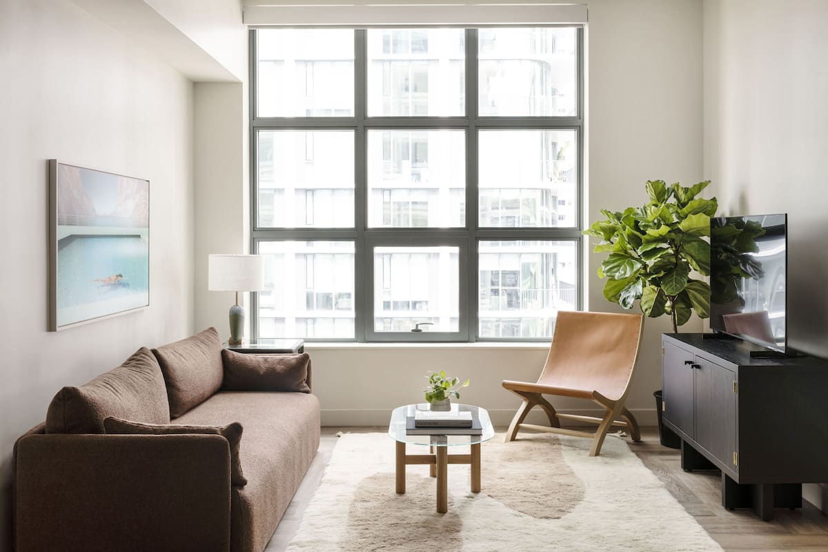 A modern living room with a large window, a sofa, a coffee table, a chair, a TV, and a plant.