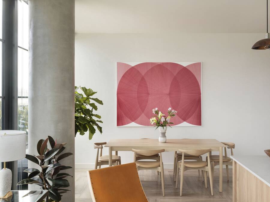 Uma sala de jantar moderna com uma mesa de madeira, cadeiras, um vaso com flores e um grande quadro abstrato na parede.
