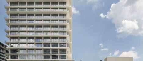 A modern hotel with a large pool area, multiple floors, and a clear sky.