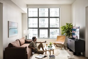 A modern living room with a large window, a sofa, a coffee table, a TV, and a bookshelf.