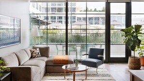 A modern living room with a sofa, a chair, a coffee table, and a large window offering a view of a balcony with outdoor furniture. - ROOST Tampa (Tampa)