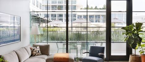 A modern living room with a sofa, a chair, a coffee table, and a large window offering a view of a balcony with outdoor furniture.