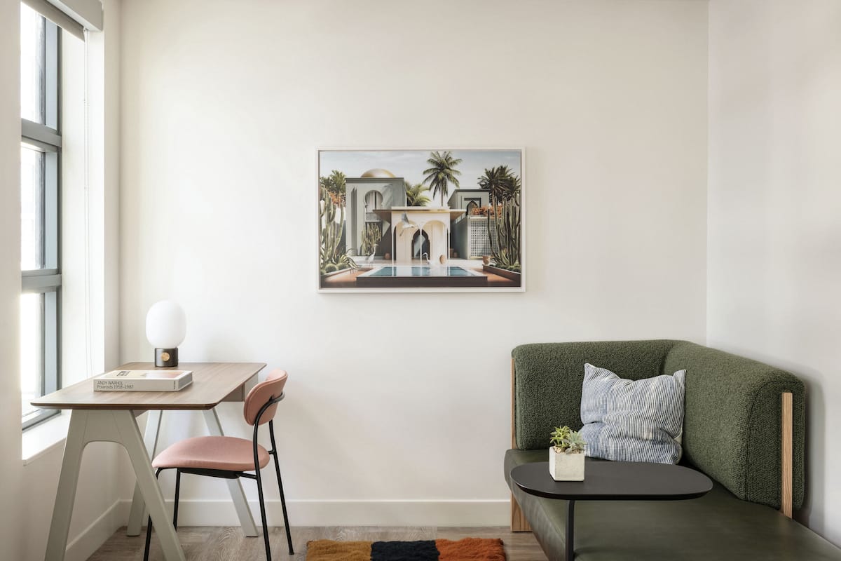 A modern living room with a green sofa, a small table with a lamp, a chair, and a framed painting on the wall.