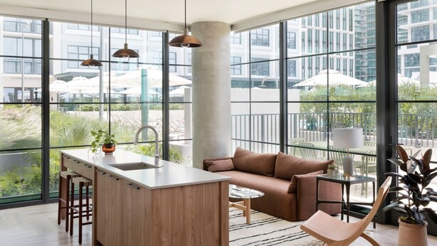 A modern kitchen with a central island, bar stools, and a seating area with a sofa and chairs. - ROOST Tampa (Tampa)