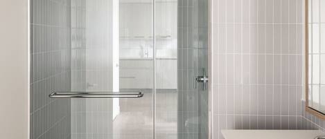 Un baño moderno con ducha envuelta en vidrio, un lavamanos blanco y muebles de madera.