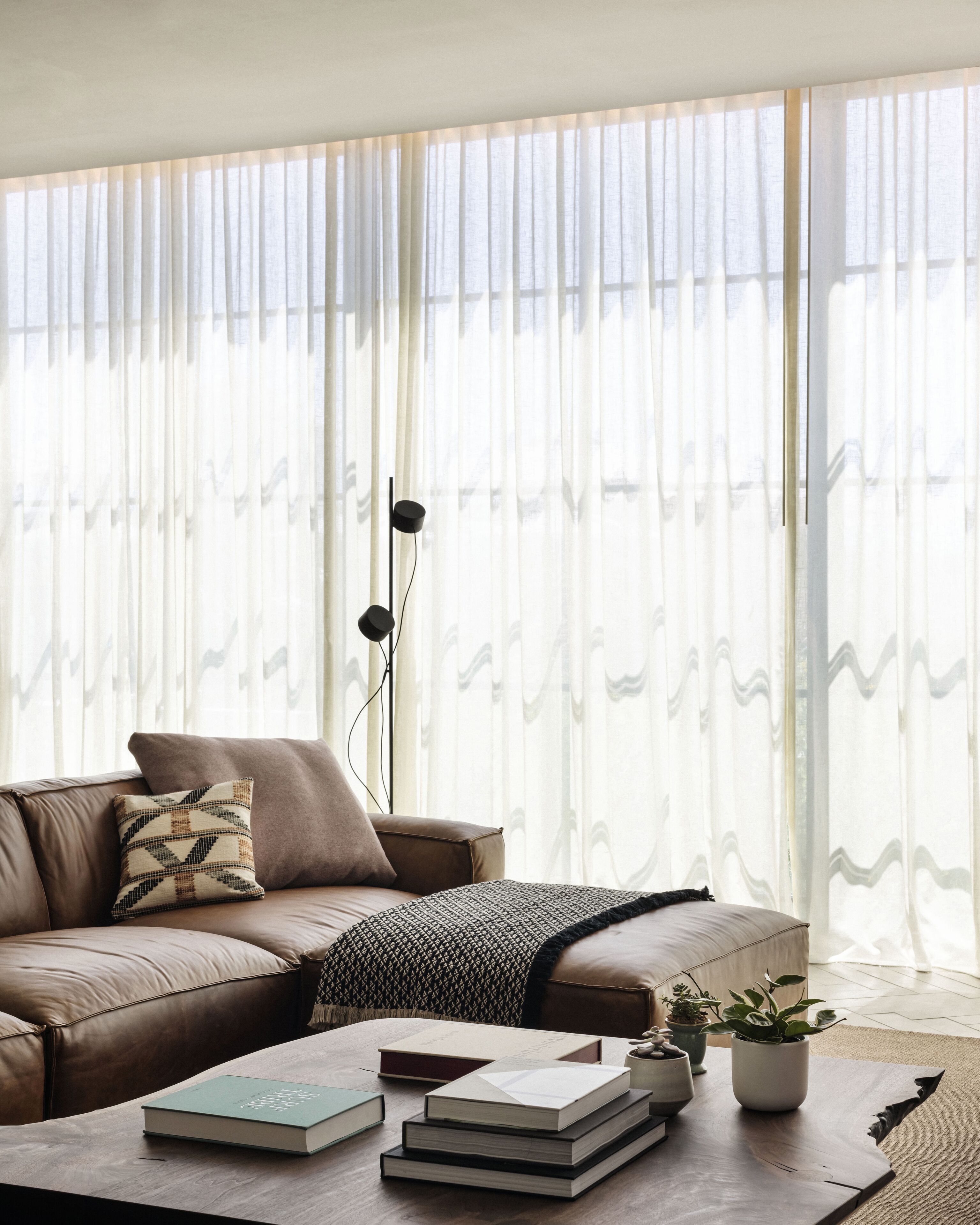 A modern living room with a leather sofa, a coffee table with books, and a floor lamp.
