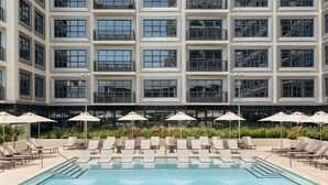 A modern hotel with a rooftop pool area, featuring sun loungers and umbrellas, and a large building with numerous windows in the background. - ROOST Tampa (Tampa)