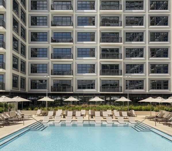 A modern hotel with a large pool area, multiple balconies, and outdoor seating with umbrellas.