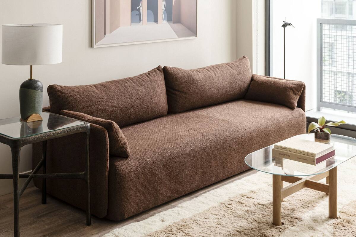 A modern living room with a brown sofa, a glass coffee table, a lamp, and a framed picture on the wall.