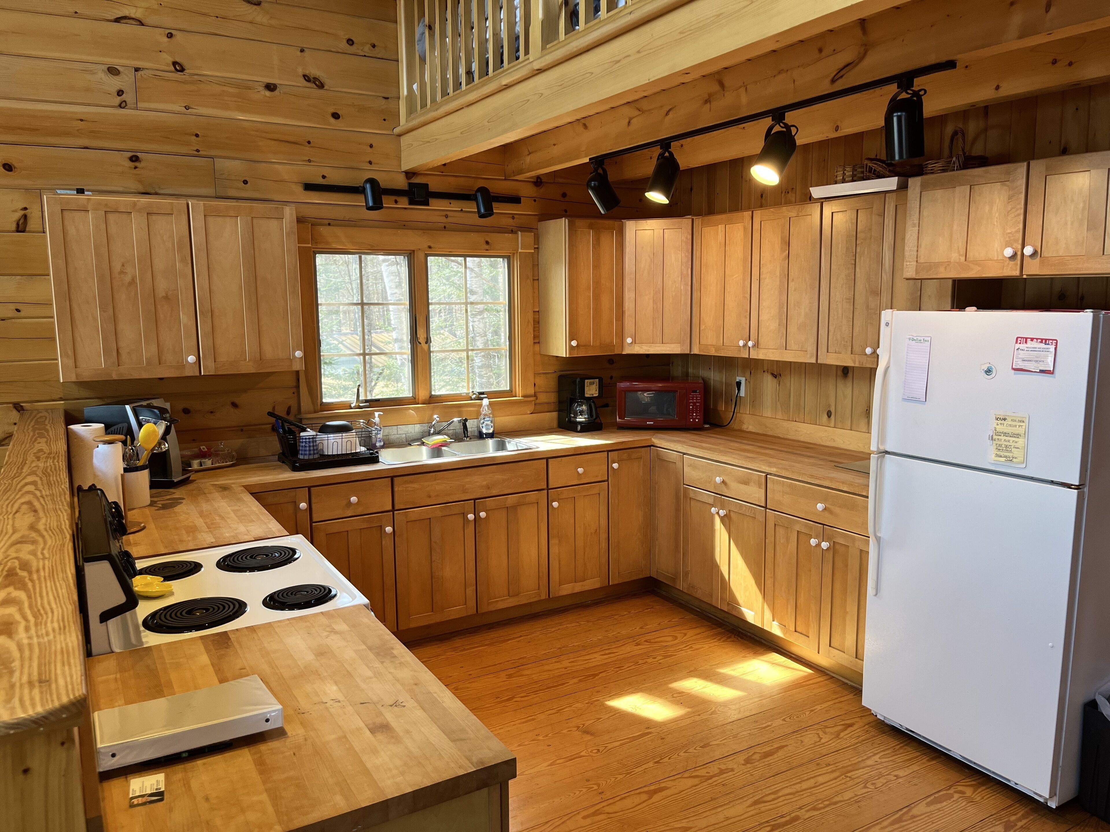 A cabin-style kitchen with wooden cabinets, a white refrigerator, a stove, and a window.