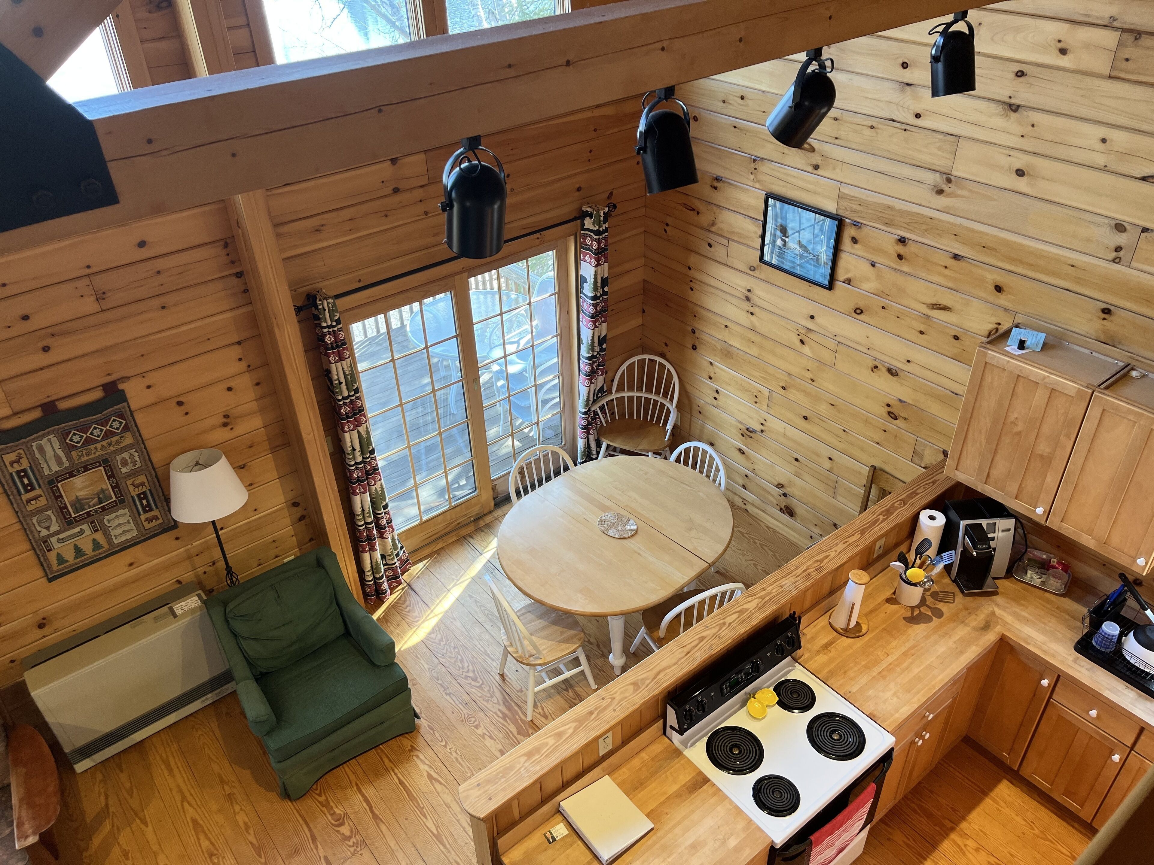 Una cocina acogedora de estilo cabaña con interior de madera, una mesa de comedor con sillas, una estufa y una ventana con cortinas.