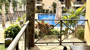 Un balcon d’hôtel avec une piscine, des chaises longues et des plantes tropicales.