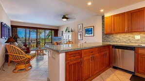 A modern kitchen with wooden cabinets, a stainless steel dishwasher, and a large island. - Ocean View, 2 Way Split AC, King Bed, Pool & WiFi (Kihei)