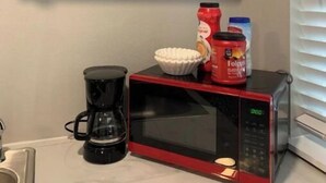 Une cuisine équipée d’un four à micro-ondes, d’une machine à café et d’étagères où sont rangées des assiettes, des couteaux et une plante.