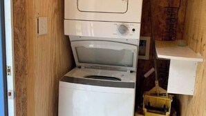 Une petite buanderie équipée d’un lave-linge et d’un sèche-linge à chargement frontal, d’une petite étagère et d’une poubelle jaune.
