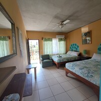 Habitación de hotel con dos camas individuales, ventilador de techo, una mesita pequeña y un banco.