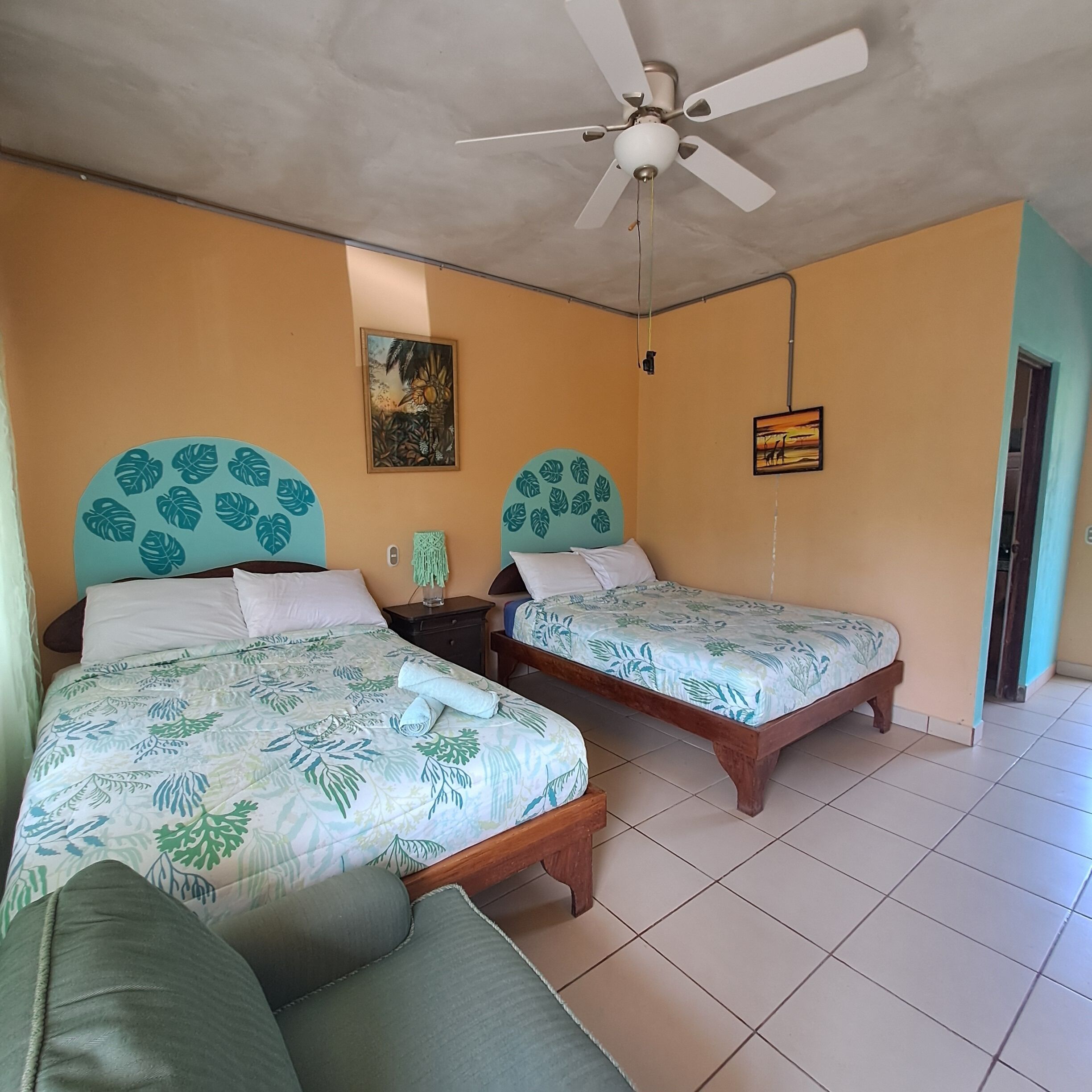 A room with two wooden beds, a ceiling fan, and a painting on the wall.