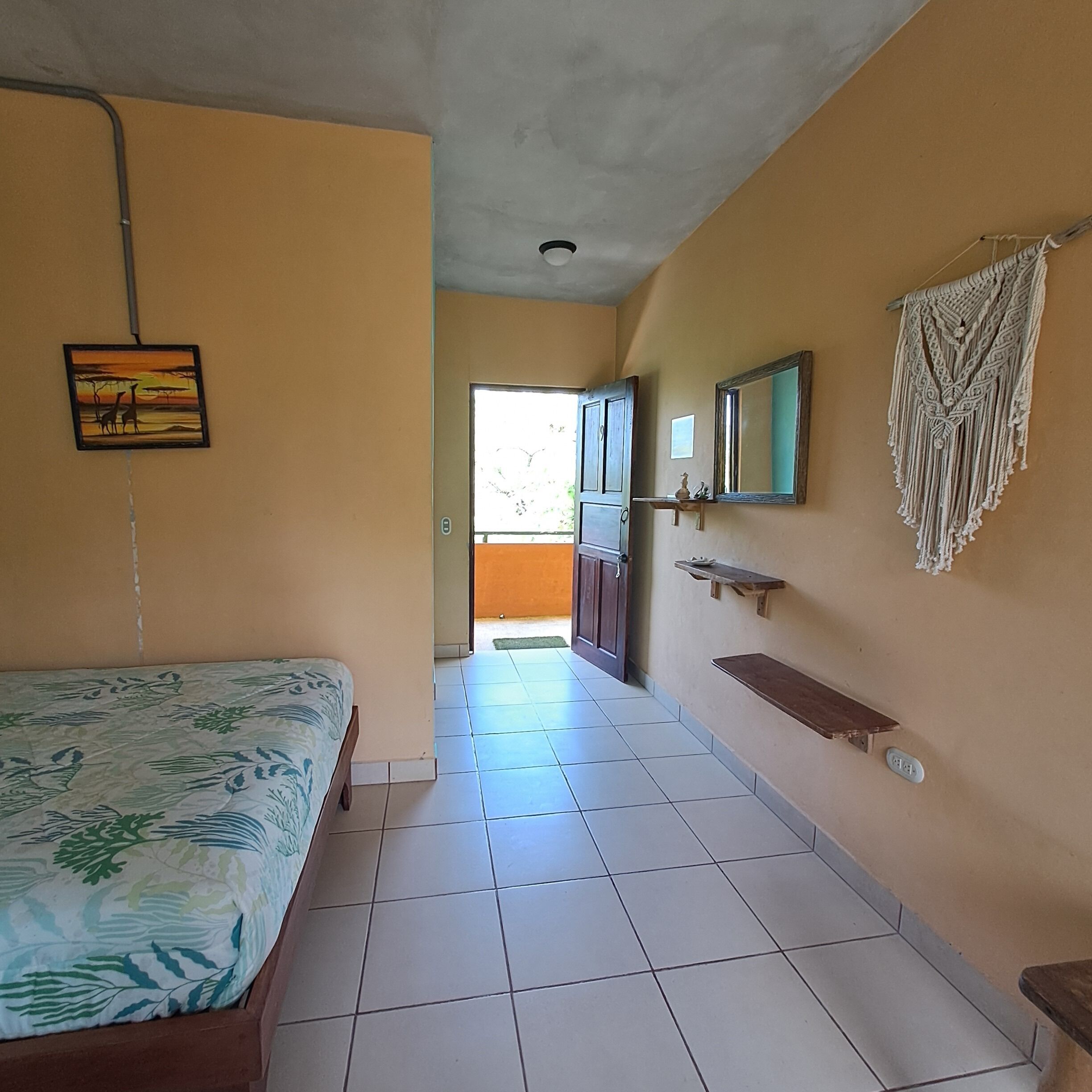 Une chambre avec un lit, une salle de bain avec un lavabo et un miroir, et un couloir menant à un espace extérieur.