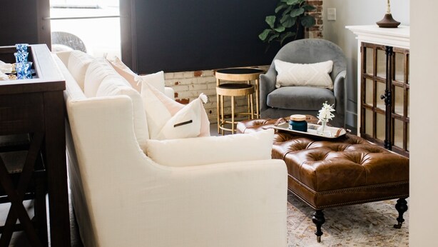 A living room with a white sofa, a brown leather ottoman, a grey armchair, a small wooden table, and a lamp. - Luxury loft in historic downtown Tifton, Georgia (Tifton)