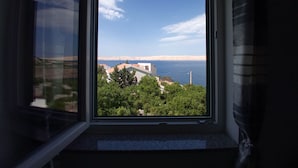 Janela com vista para paisagem costeira, incluindo edifícios e o mar.